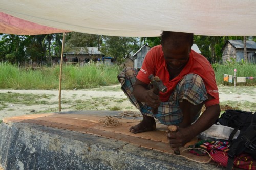 Madhab continues to repair the boat he is working on with his chisel and hammer, under the shade from the sun.