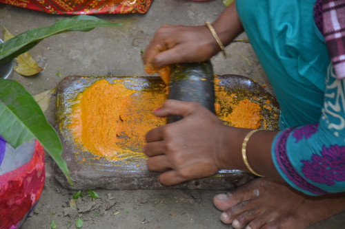 Women crushing turmeric with a traditional mortar and pestle in preparation for cooking the food.