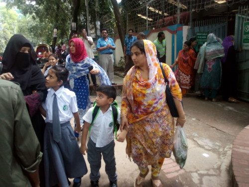 Two parents wait for their vehicle to arrive in front of a school in Dhaka